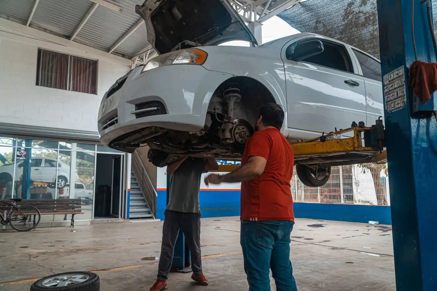 Two mechanics inspecting a white car on a lift inside a garage workshop