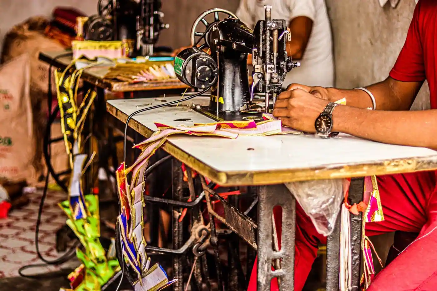 A close-up of a tailor sewing colorful fabric on an industrial sewing machine.