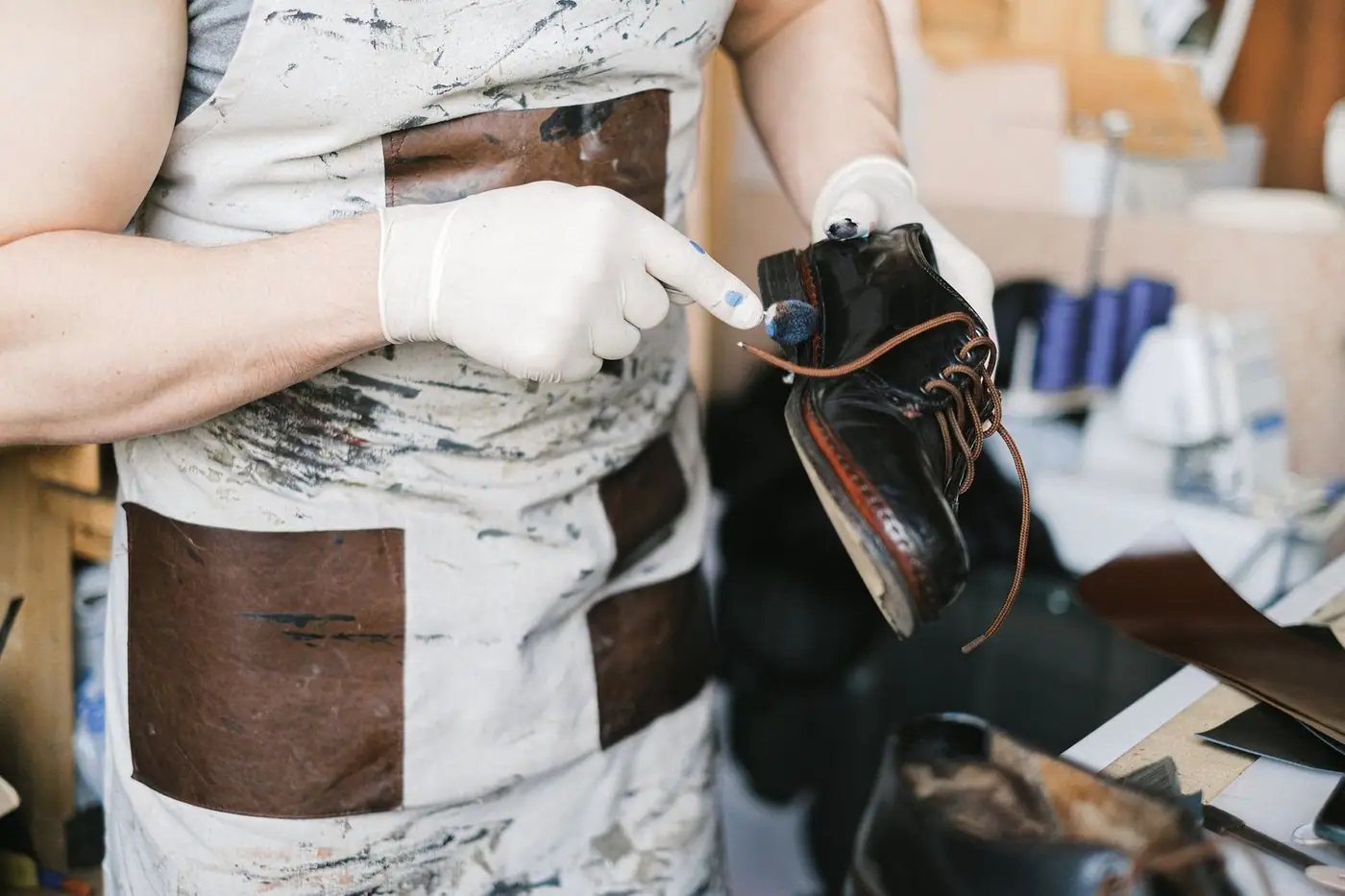 A craftsman in gloves polishing black leather shoes at a workbench.