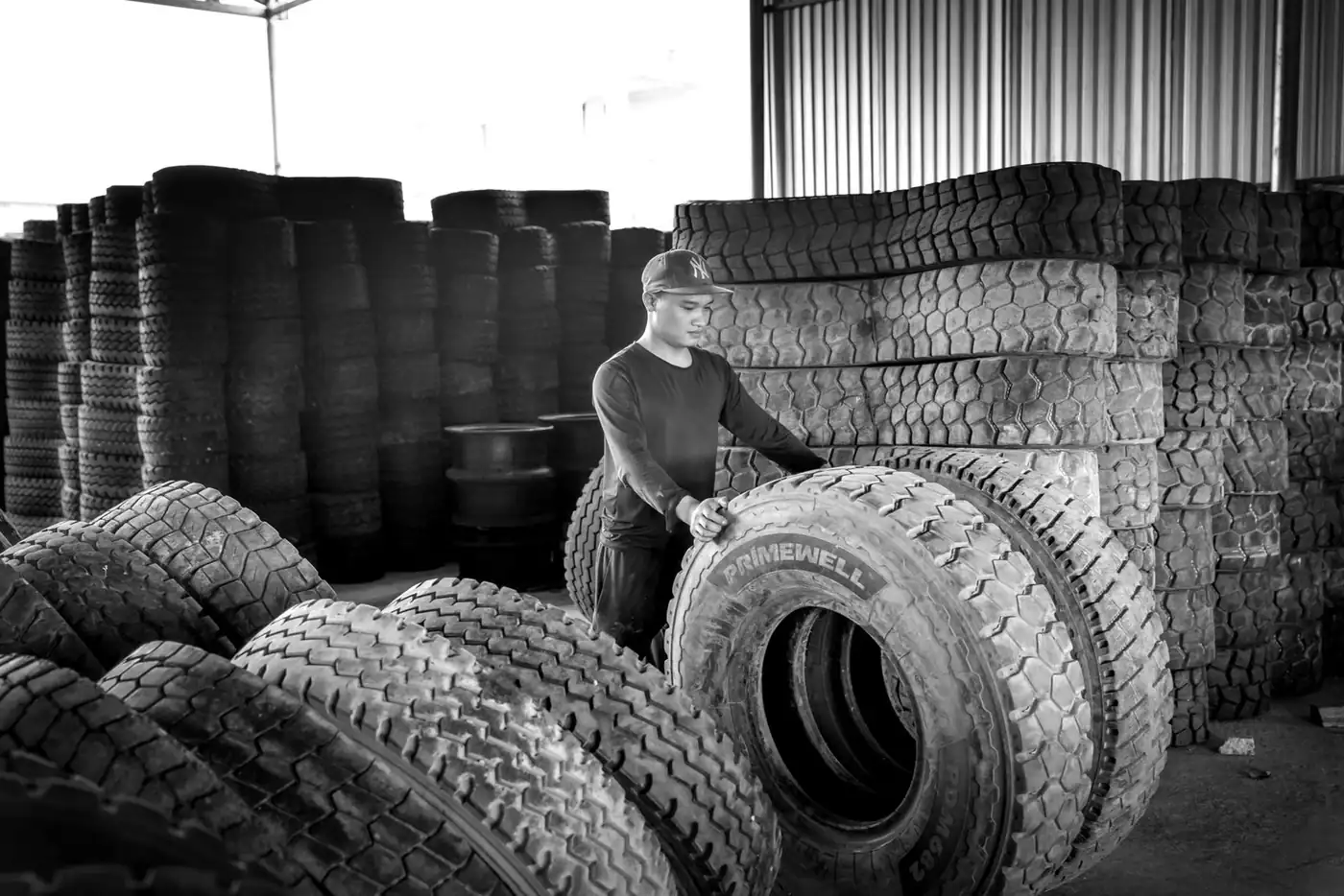 Black and white photo of a man stacking large tyres in an industrial warehouse