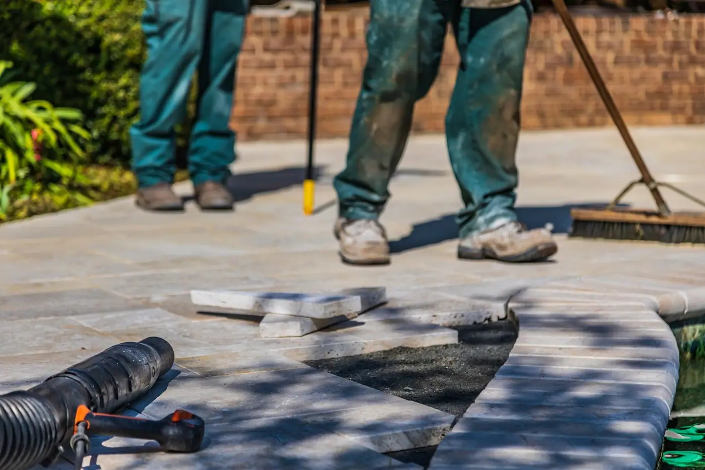 Workers laying tiles on an outdoor patio under sunlight