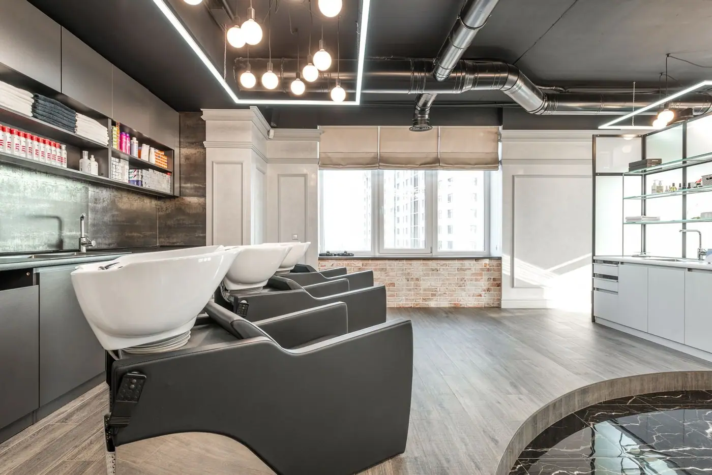 Black backwash chairs with sinks in a modern, spacious salon with a window and shelves of supplies