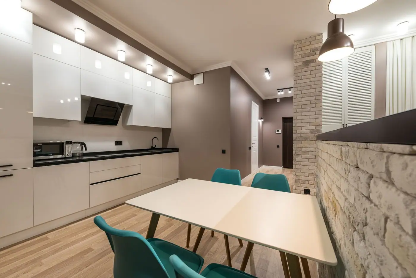 Table and chairs in a modern kitchen with white cupboards, a counter with appliances and glowing lights