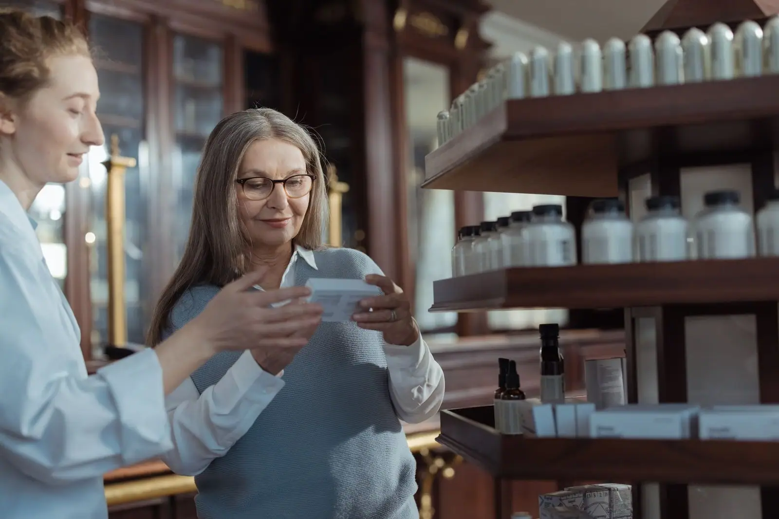 Elderly woman receiving assistance from a pharmacist in a pharmacy with product shelves