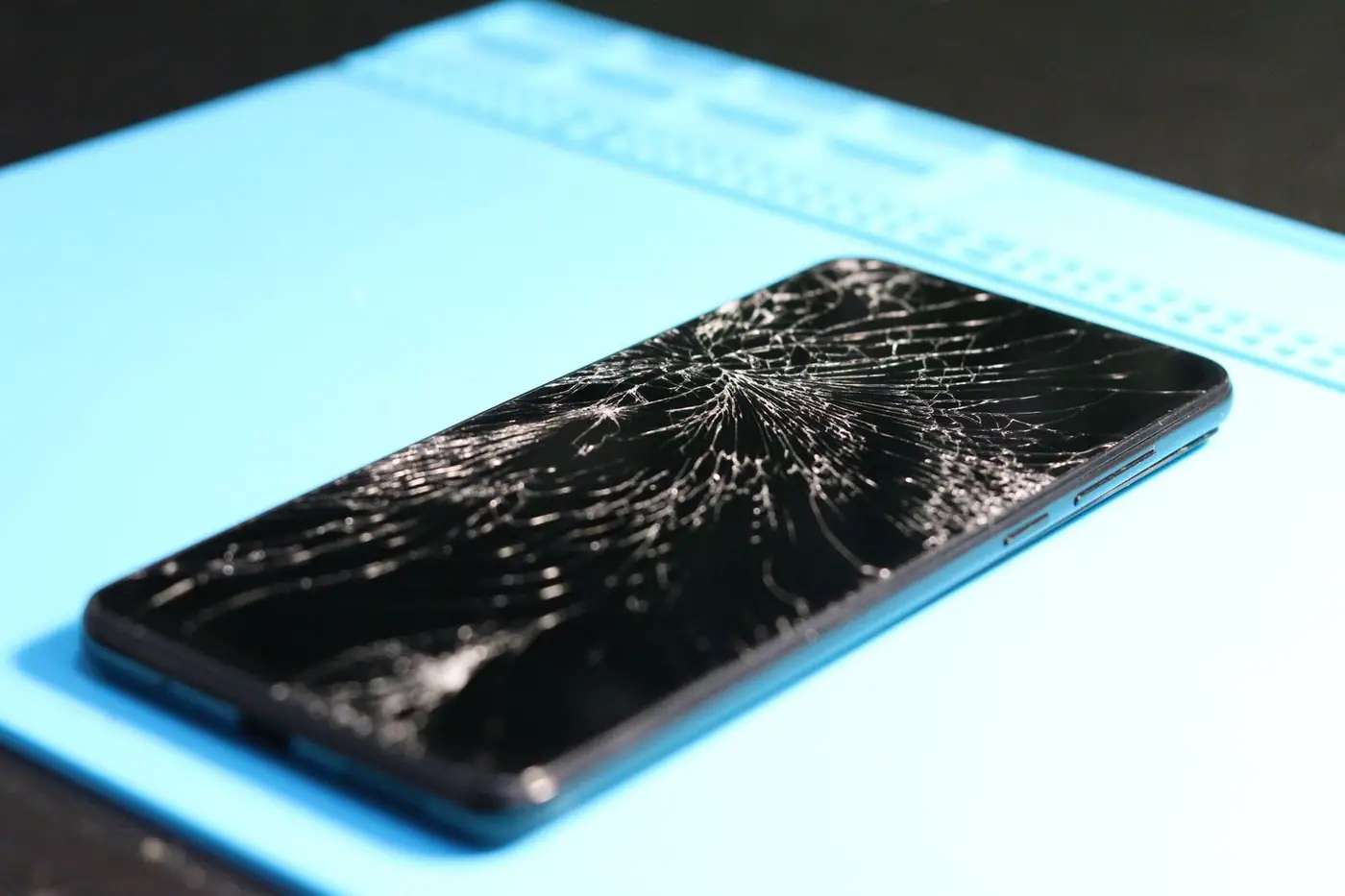 A cracked smartphone screen lying on a repair mat