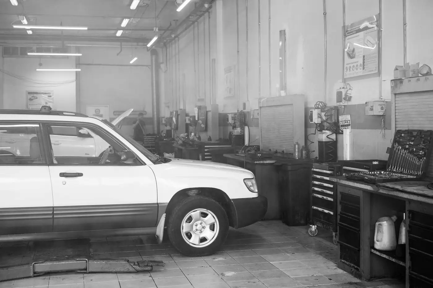Black and white image of a car in a garage surrounded by tools and equipment