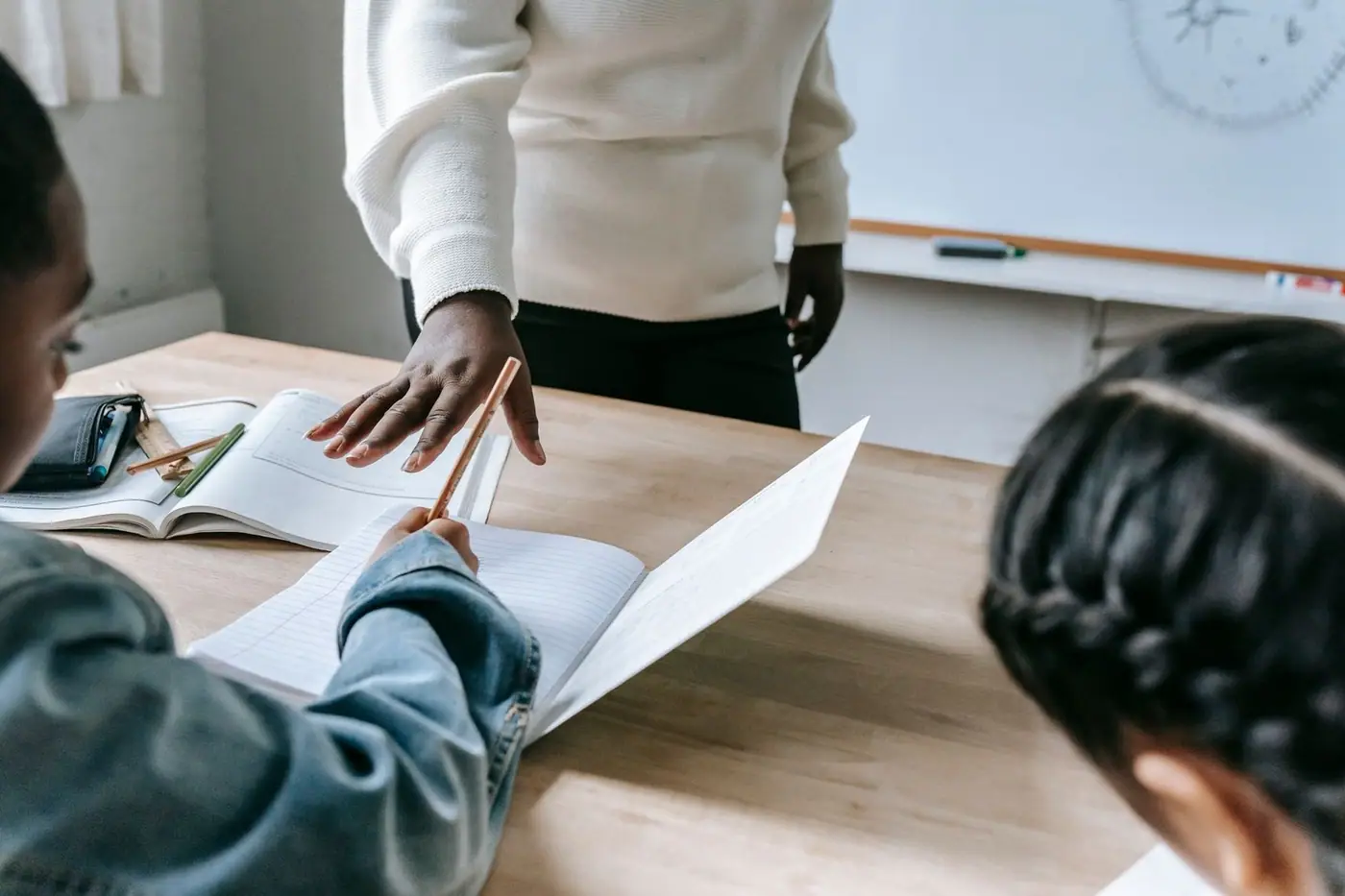 A teacher standing by a desk while students write a test with pencils in a classroom