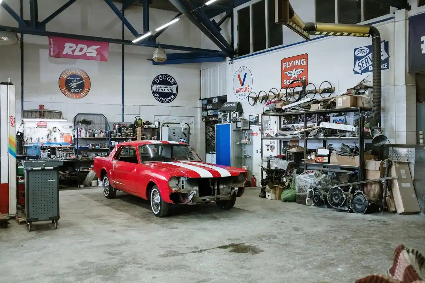 A vintage red car undergoing restoration in a well-equipped workshop with various tools and auto parts
