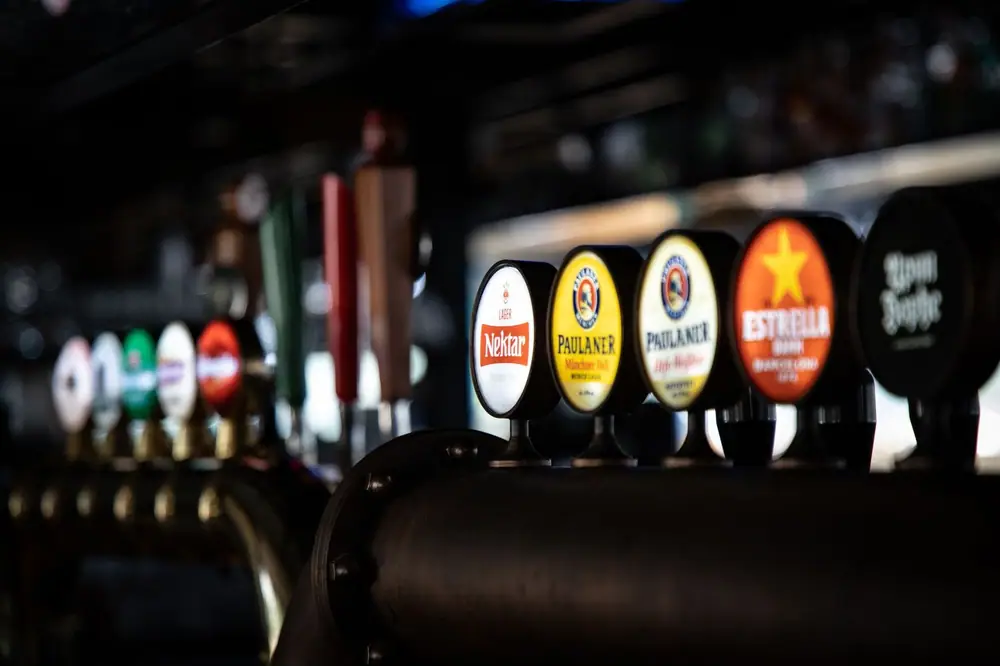 Close-up of assorted beer taps in a dimly lit bar, showcasing various brewery logos and selections.