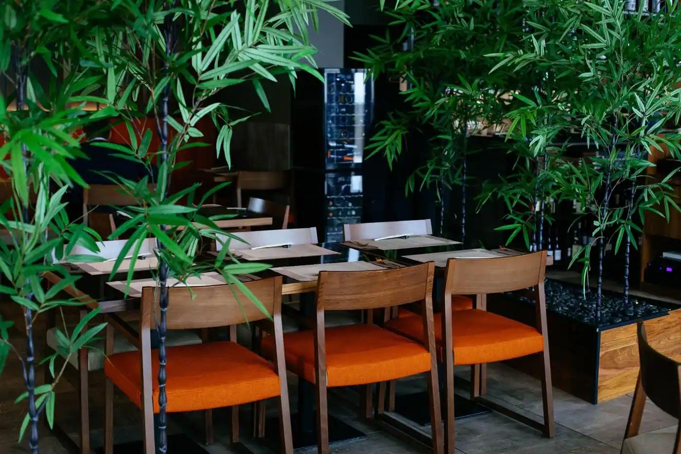 Inviting restaurant interior with orange chairs and bamboo plants, offering a calm dining atmosphere