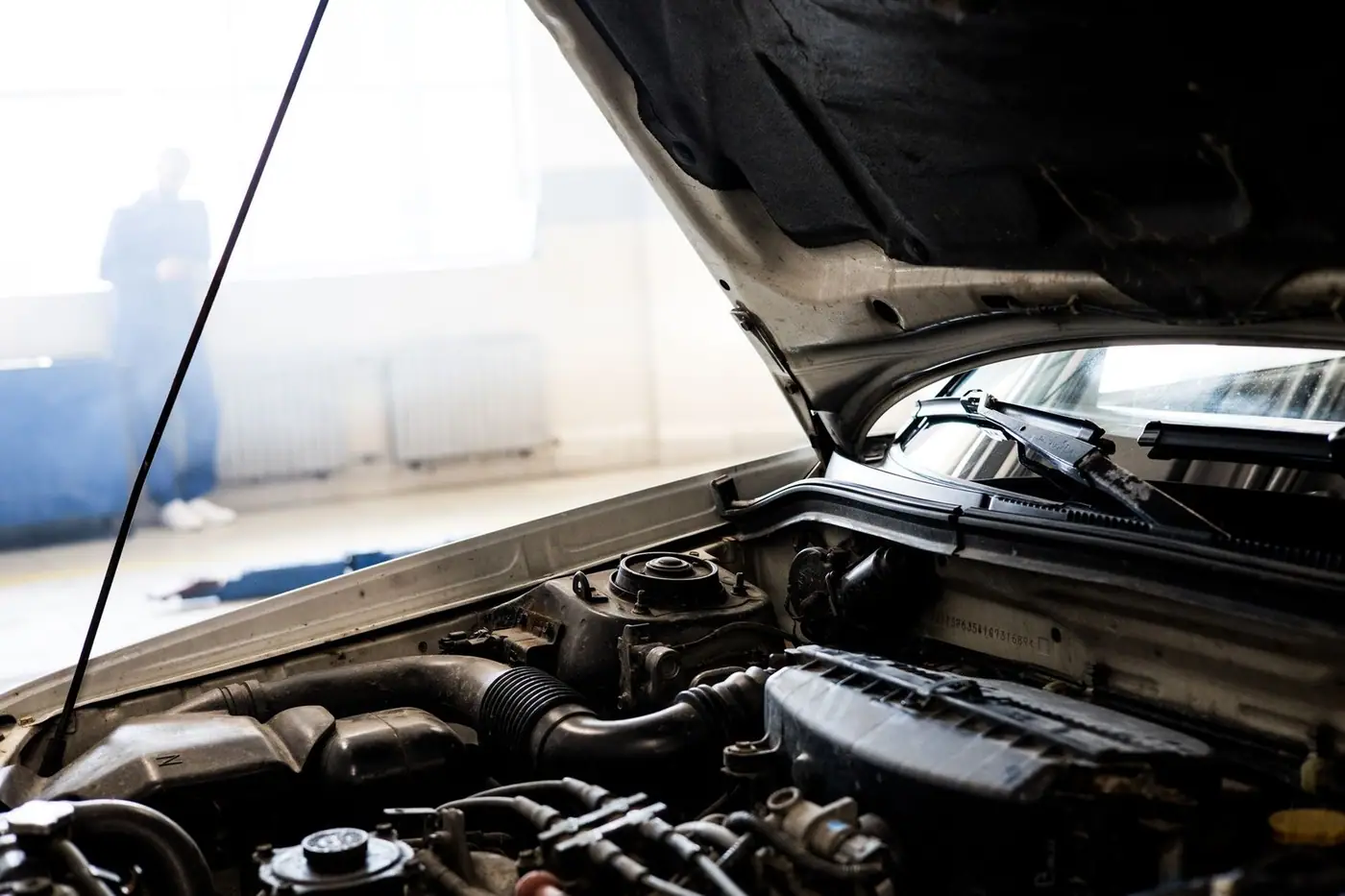 A car engine underneath an open bonnet in a well-lit garage