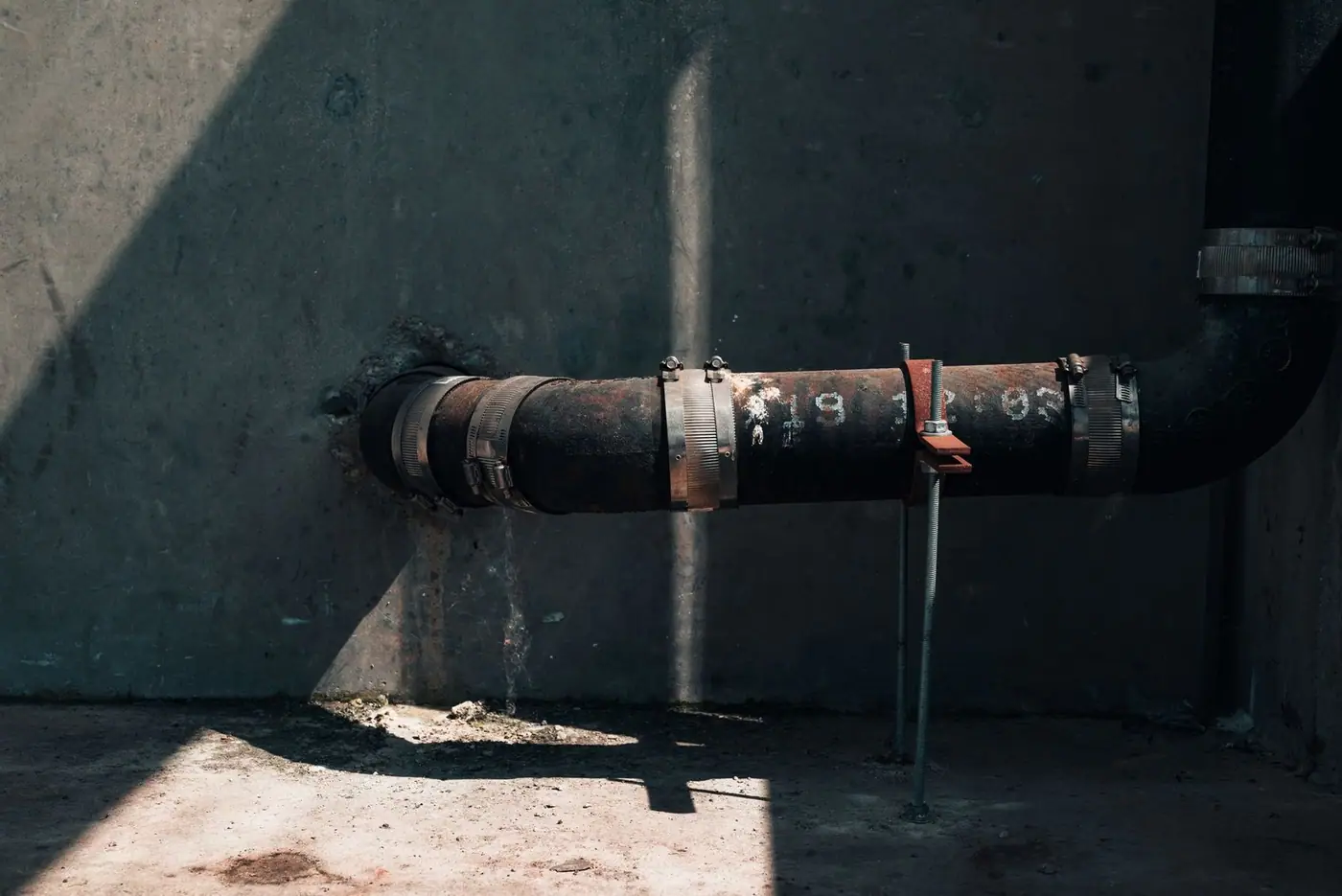 Rusted industrial pipe on a concrete wall in dramatic sunlight and shadow