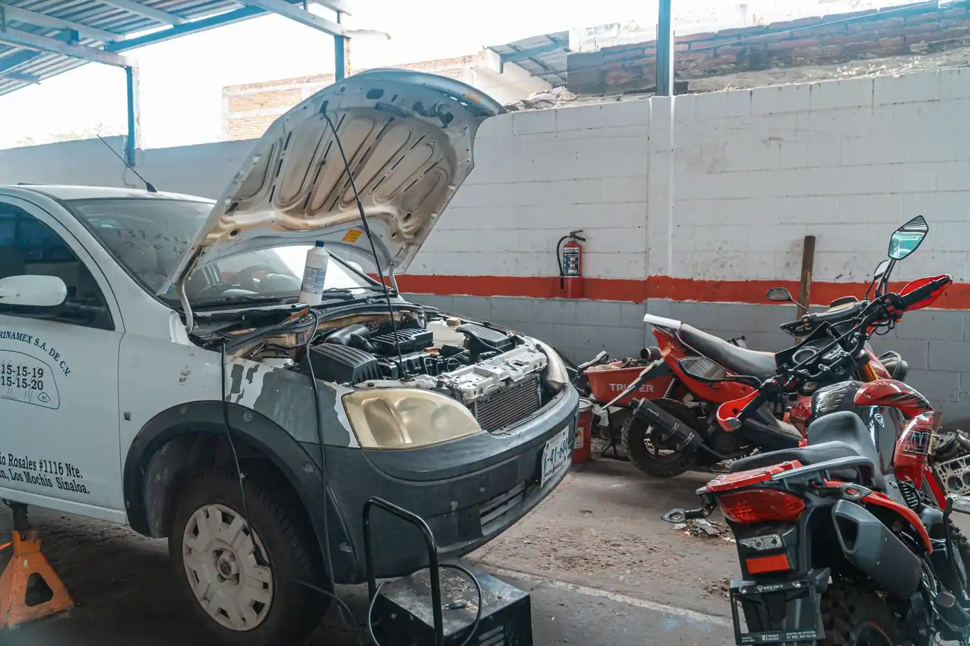 Car being repaired in a garage with motorcycles and tools around