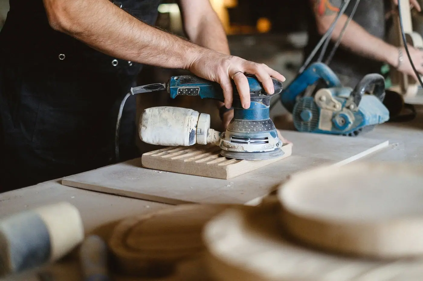 A random orbital sander smoothing a wooden board on a workbench