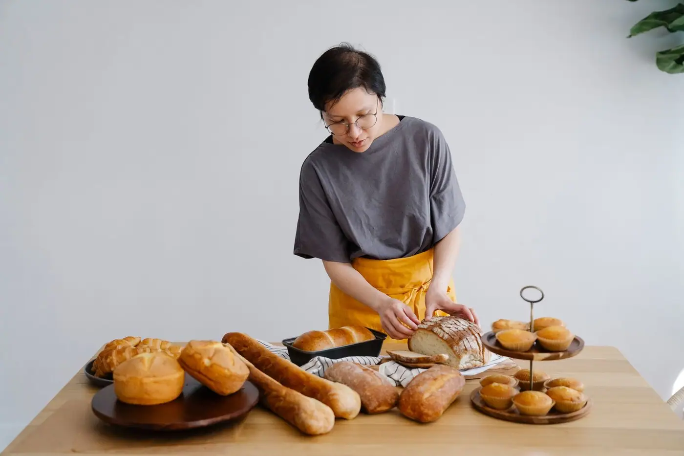 A woman wearing an apron slices freshly baked bread on a wooden table