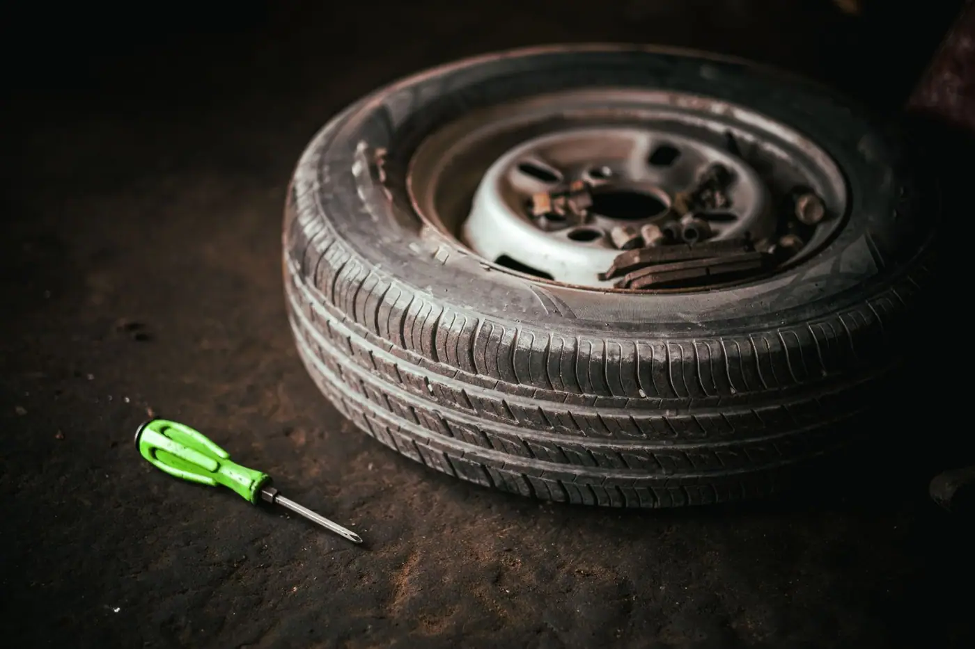 A car tyre and a green screwdriver on a garage floor