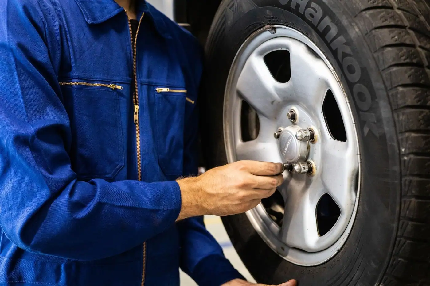 Mechanic in blue coveralls inspecting a car tyre in a workshop