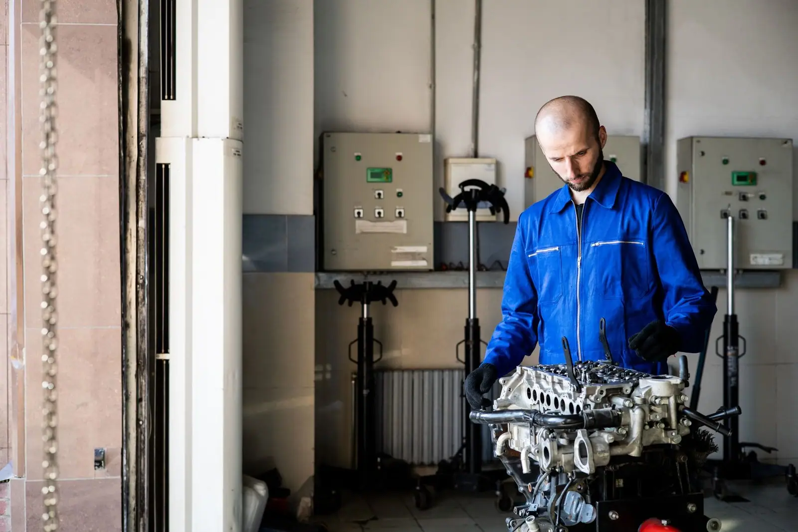 A mechanic in blue coveralls inspects an engine in a repair shop