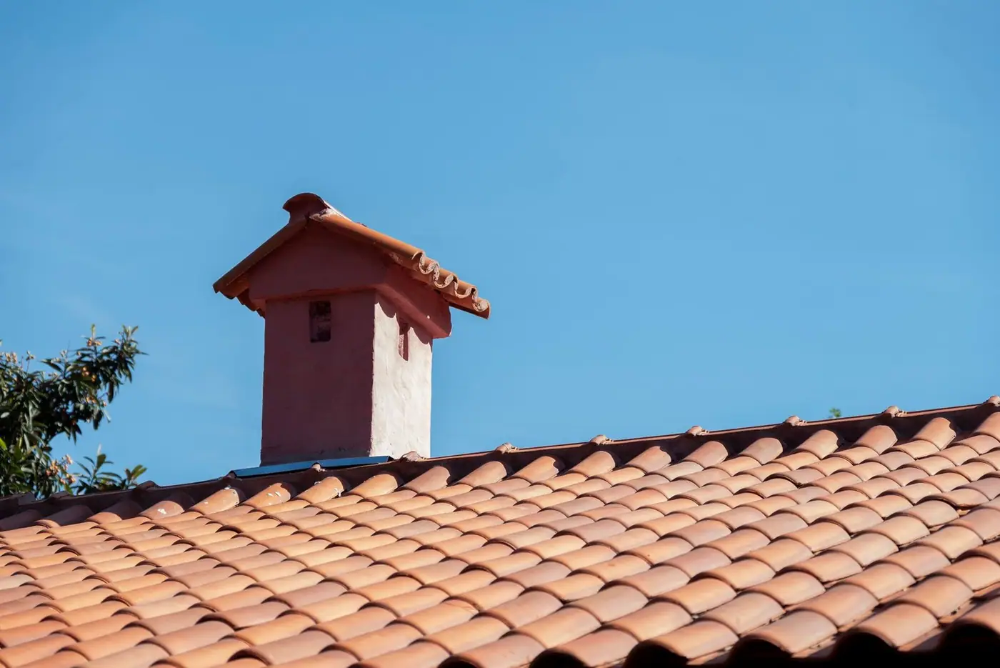 Close-up of a red tiled roof and chimney under a bright blue sky