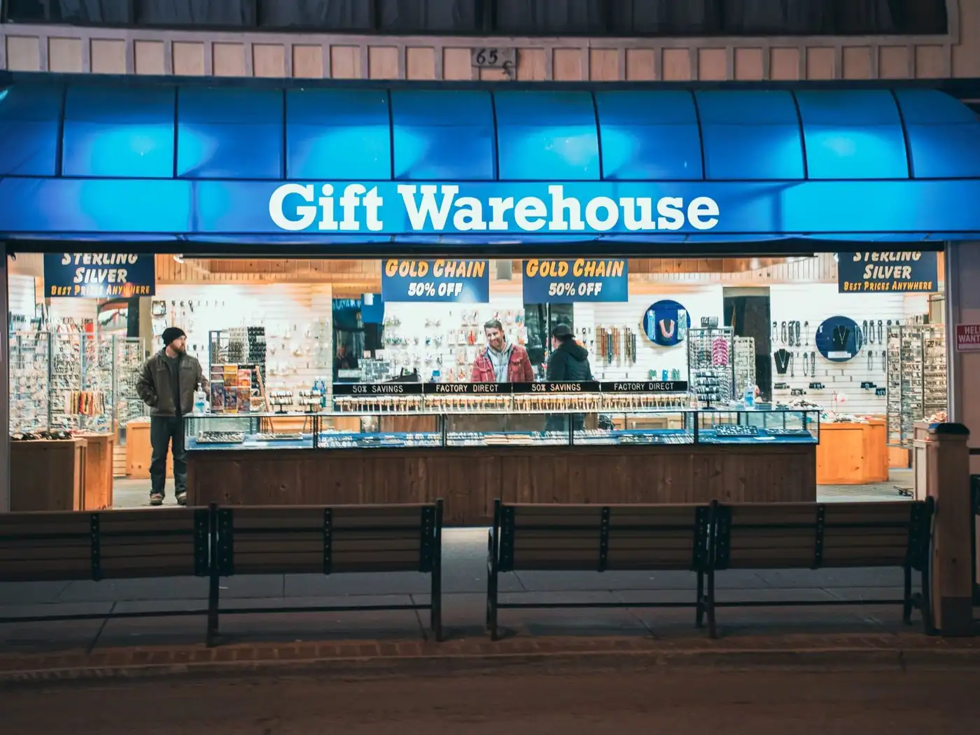 Night view of a shop with bright blue signage and two people inside.