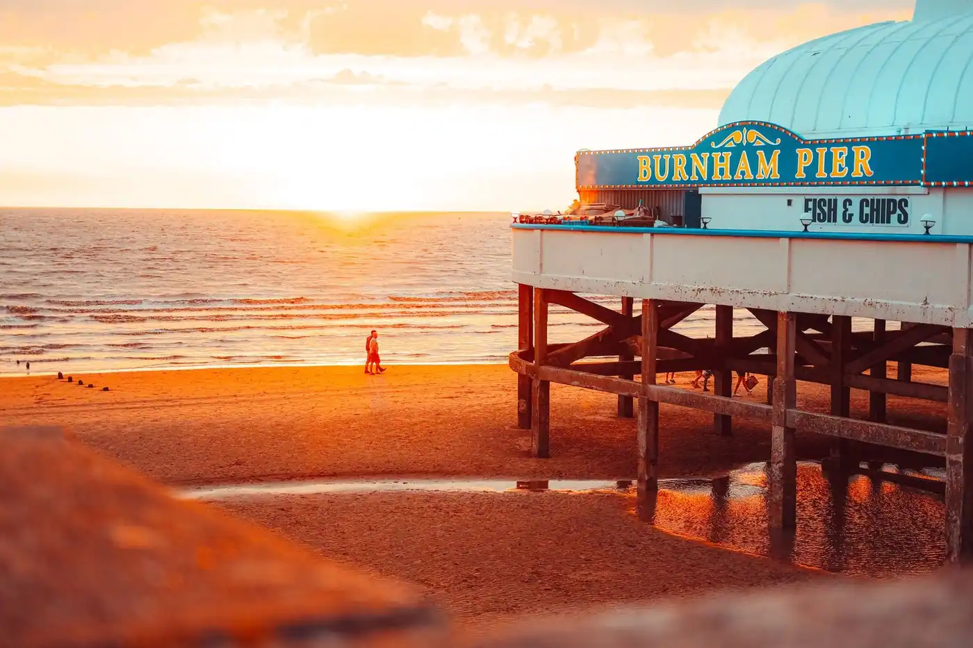 A warm sunset view over a pier, with beachgoers and the coastal horizon