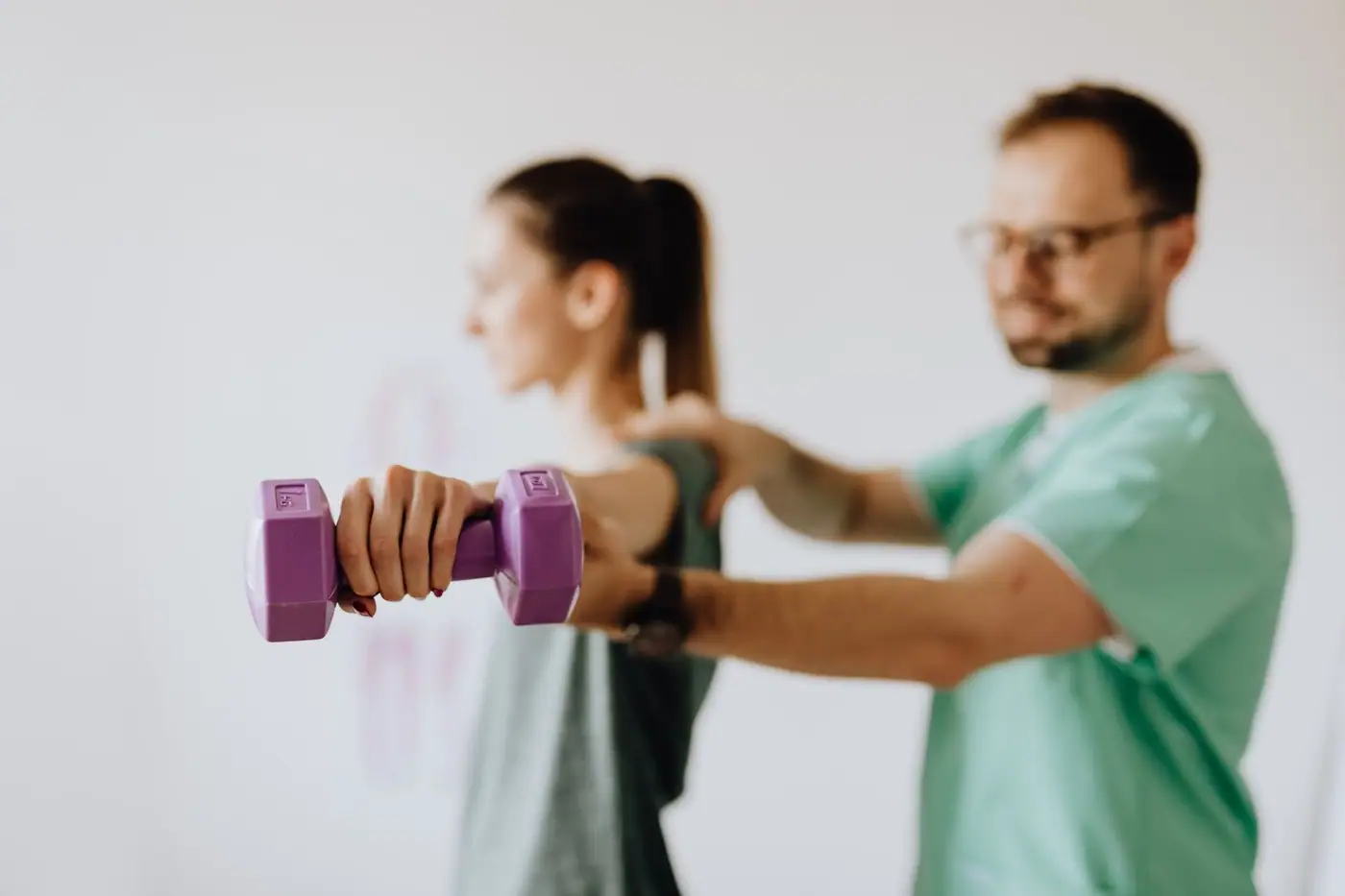A clinician in uniform and eyewear helping a woman with an arm exercise in a consulting room