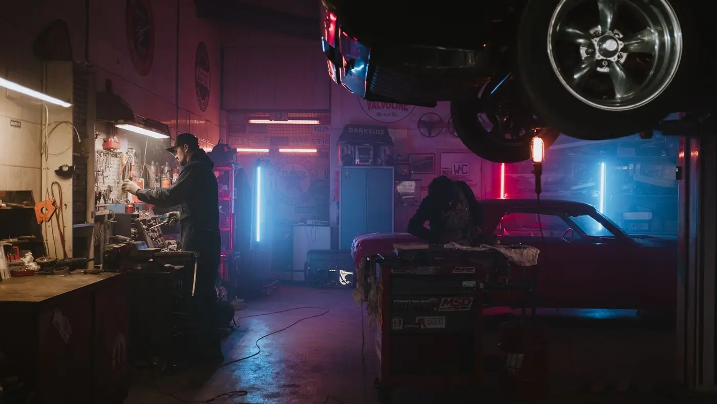 Mechanics working in a neon-lit garage, focusing on tools and car repairs under vibrant lights.