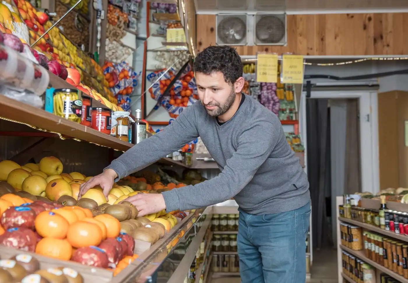 A grocery worker arranging fresh fruit and vegetables on display shelves