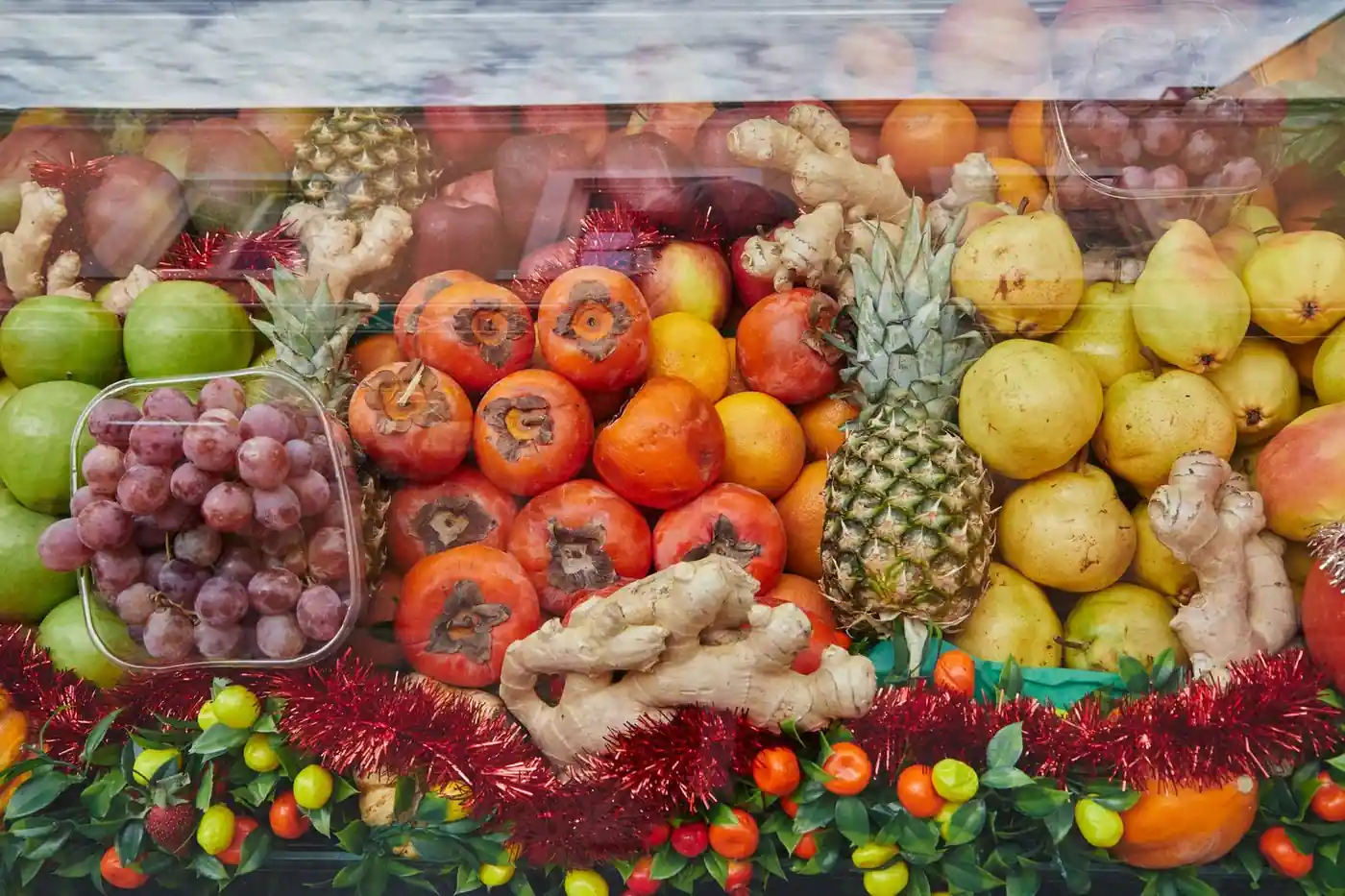 A colourful assortment of fresh fruits including pineapple, persimmons, grapes and ginger