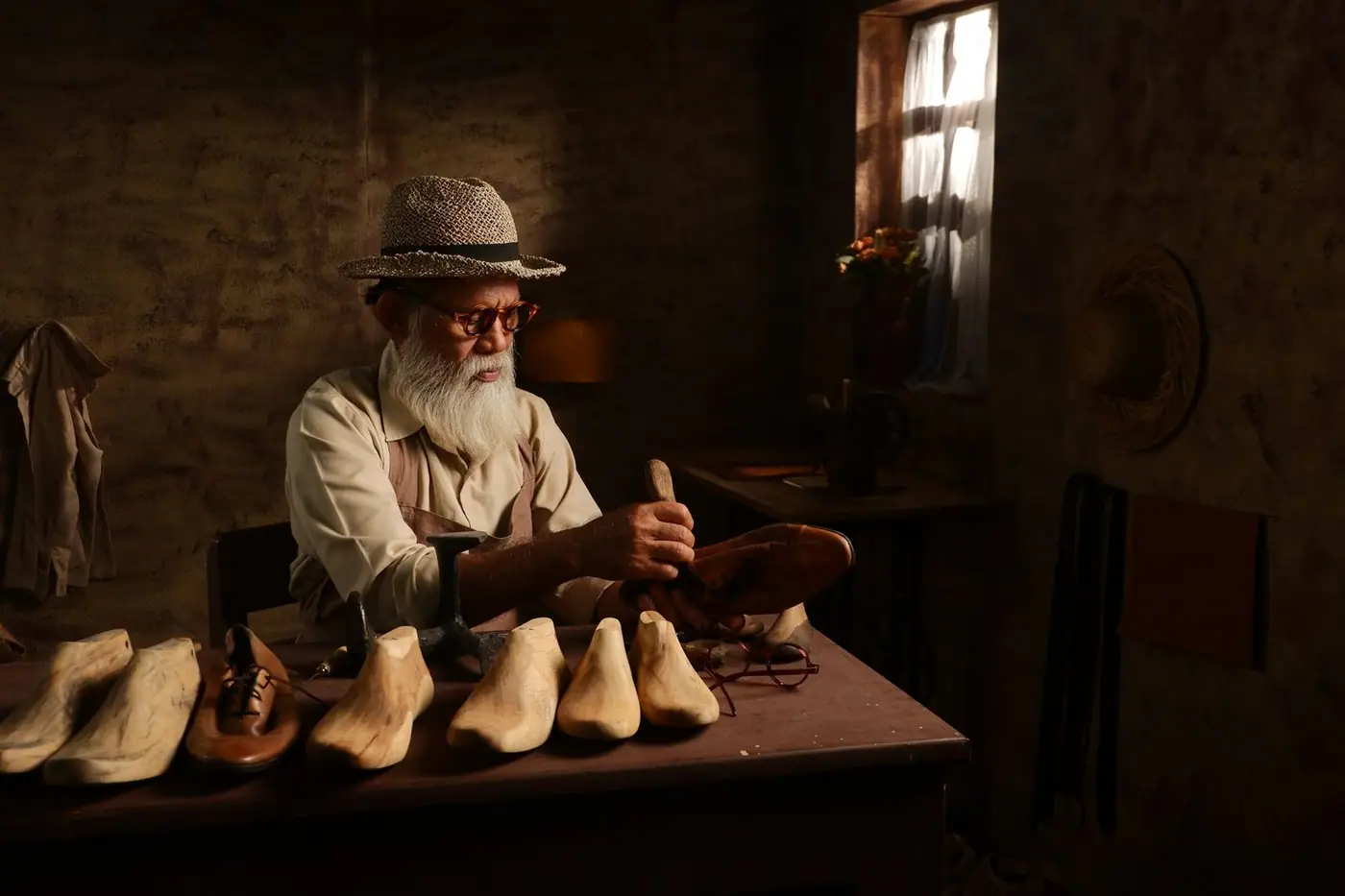 A senior craftsman working by hand at a bench surrounded by traditional tools