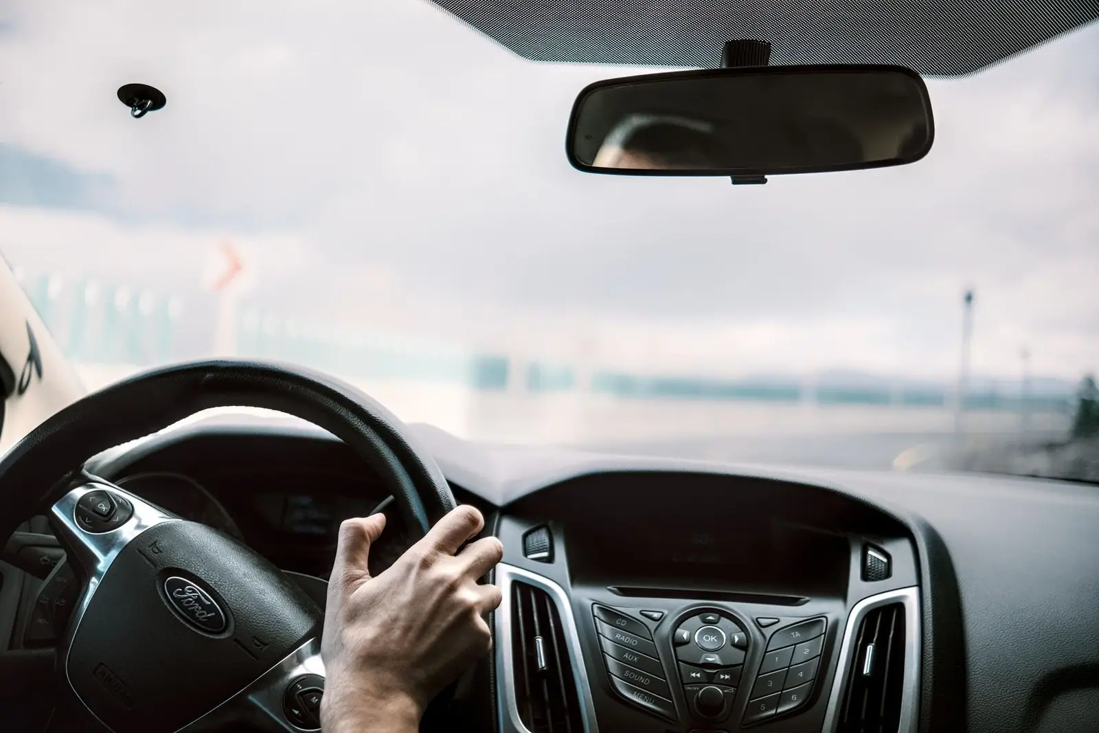 View from inside a car showing steering, rear-view mirror, and blurred road outside.