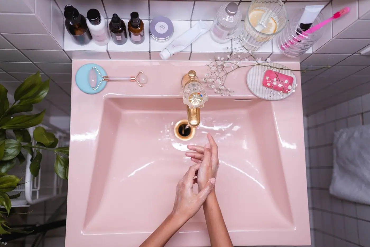 A stylish bathroom with skincare products and a person washing their hands in a pink sink
