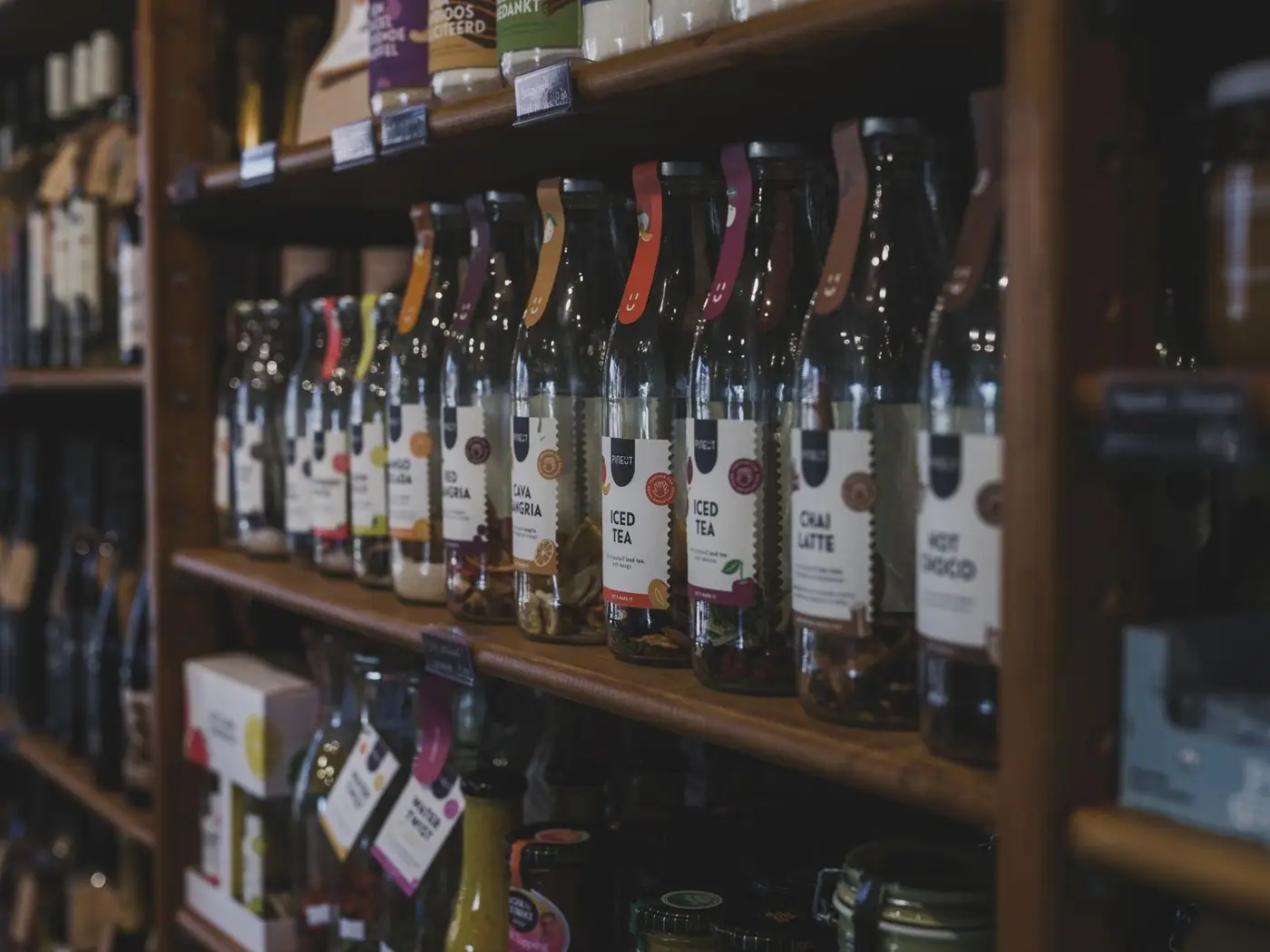 A variety of bottled beverages arranged on wooden shelves in a cosy shop setting