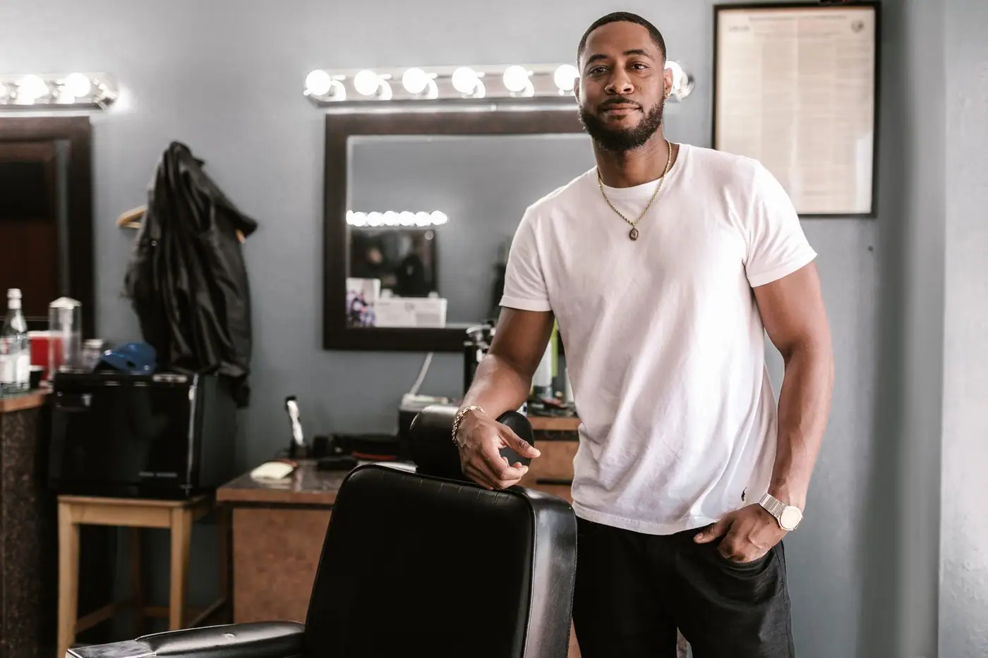 A stylish barber standing confidently by a chair in a modern barbershop