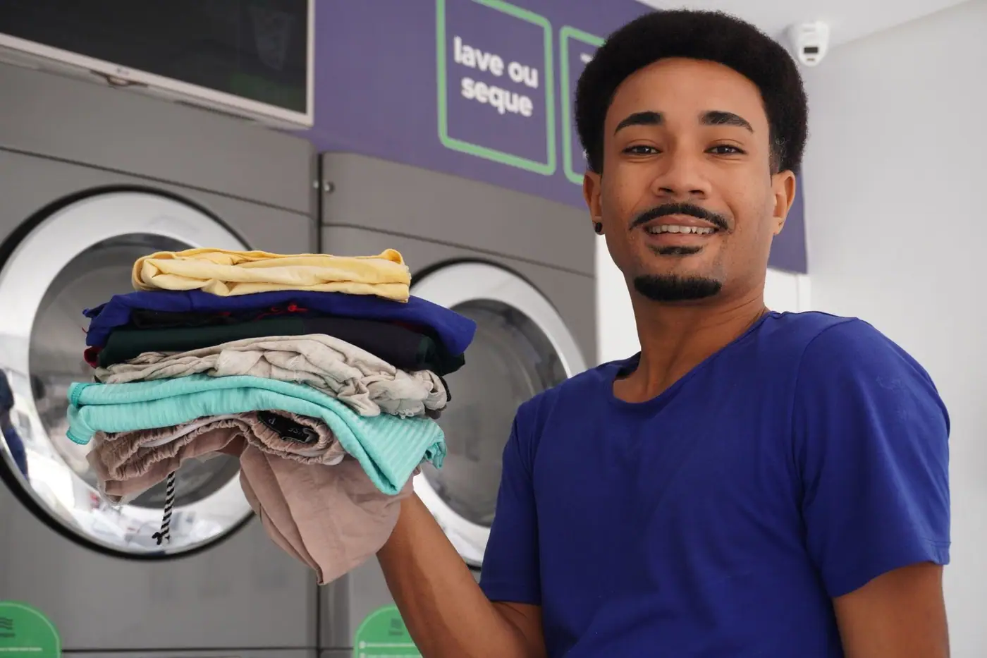 A happy man holding freshly washed clothes at a laundromat