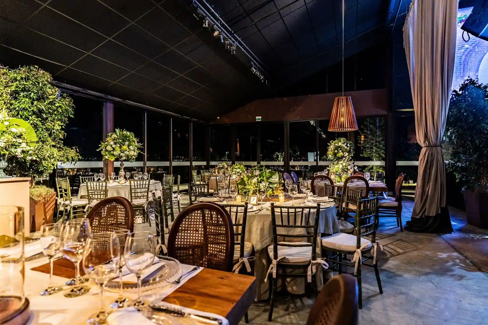 Stylish indoor restaurant setting with elegant tables and lush green decor at night.