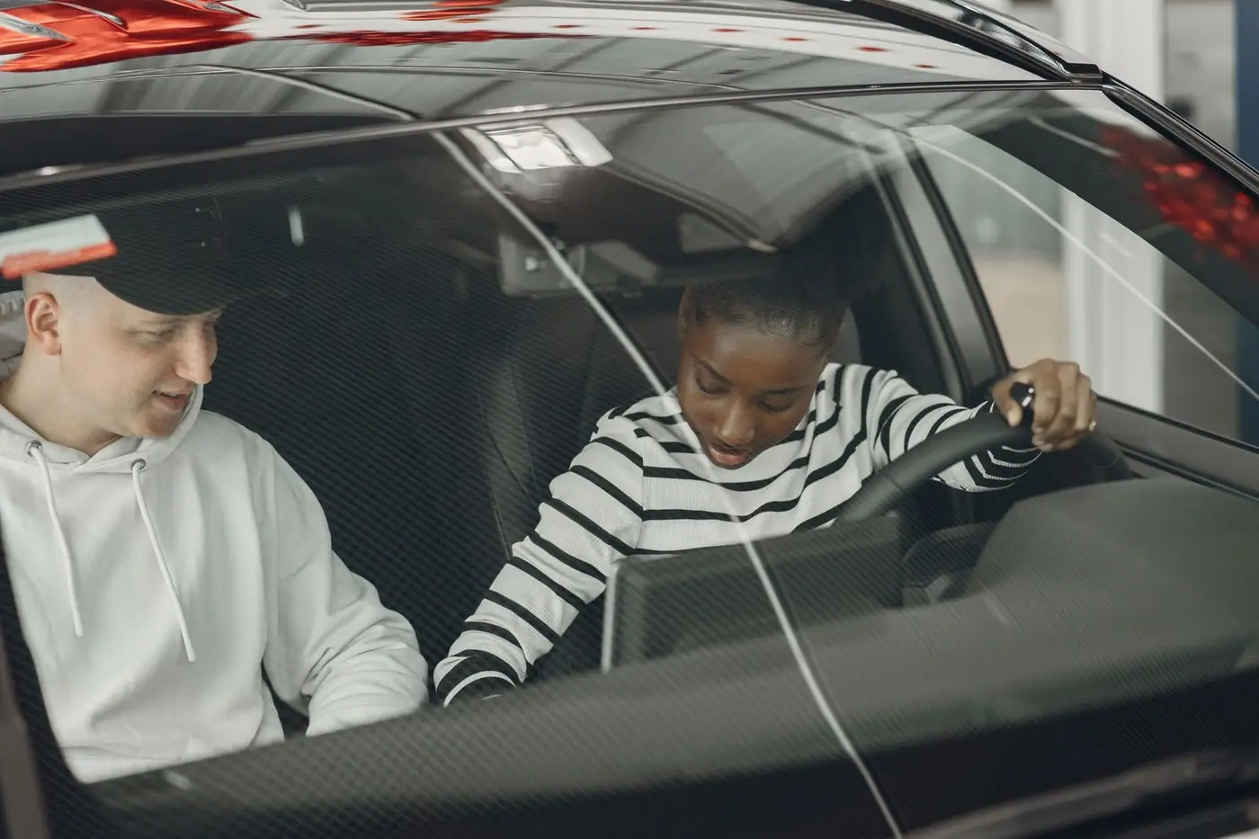 Two people sitting inside a vehicle, discussing driving.