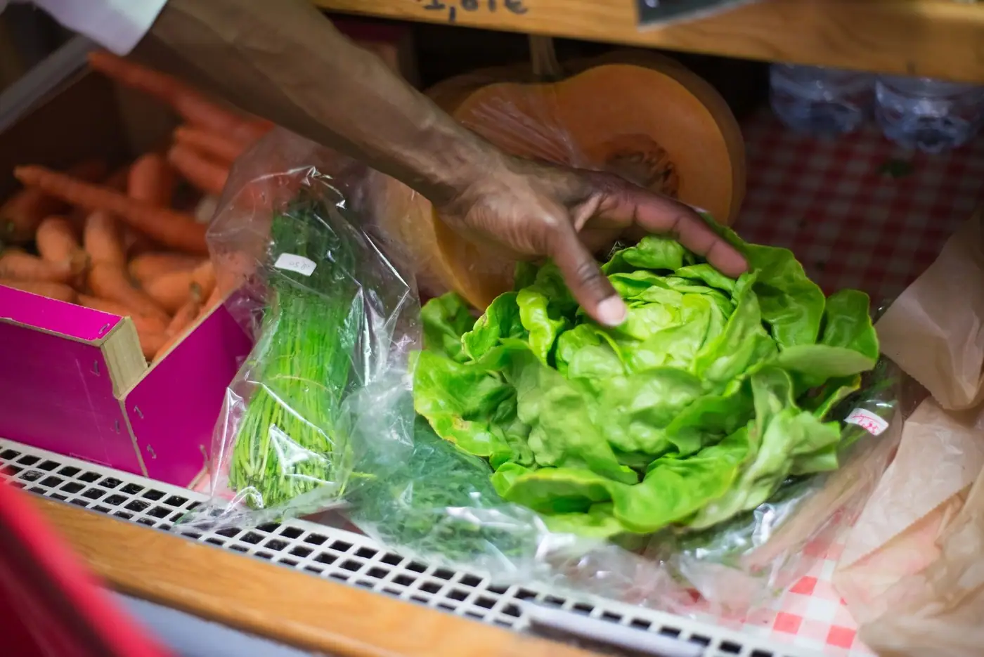 A hand picking fresh green lettuce from a shelf of vegetables