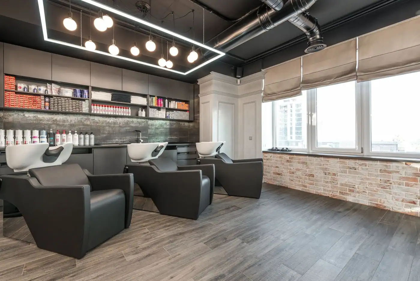 Modern leather chairs with backwash sinks in a spacious salon with windows and professional supplies on the shelves