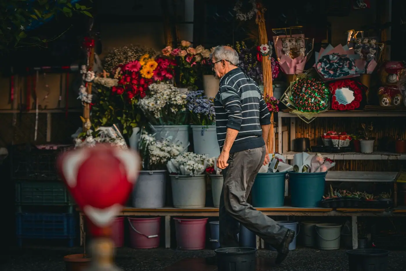 An elderly man walks past a colourful flower stall filled with vibrant bouquets and arrangements
