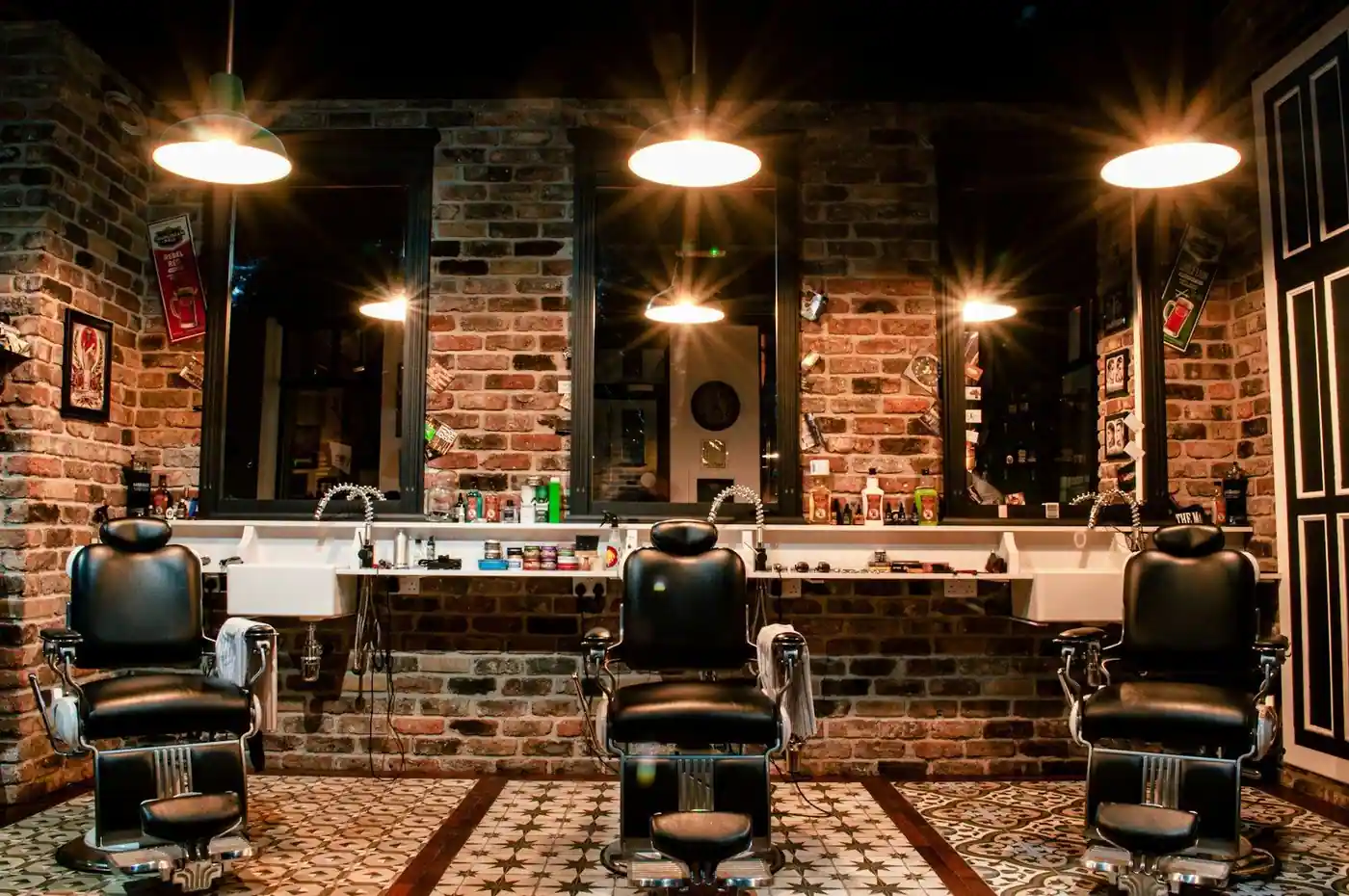 A barbershop interior with black leather chairs, exposed brick walls, large mirrors and pendant lights