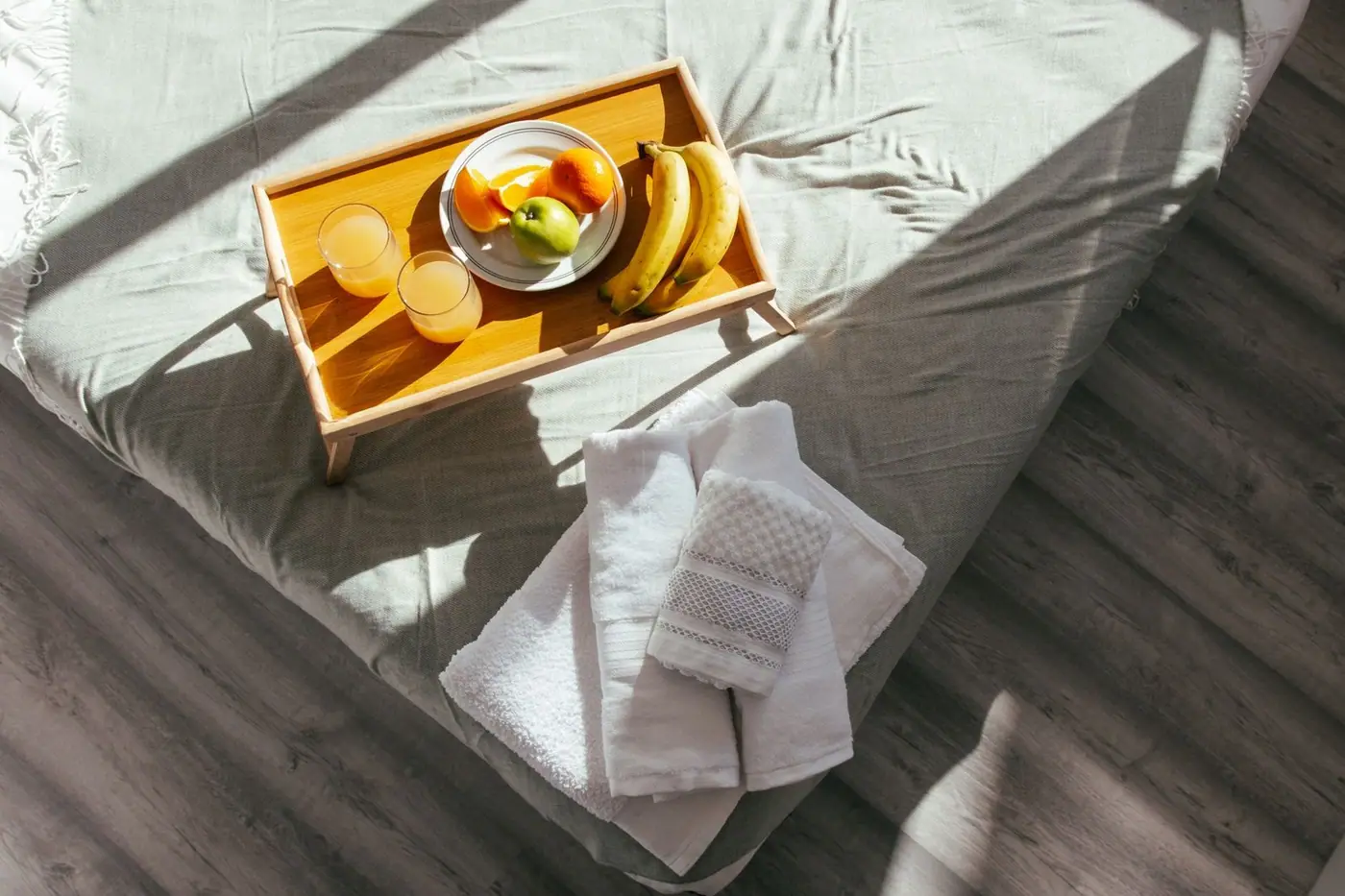 A sunlit bedroom with a fresh fruit breakfast tray and neatly folded towels on a soft bed