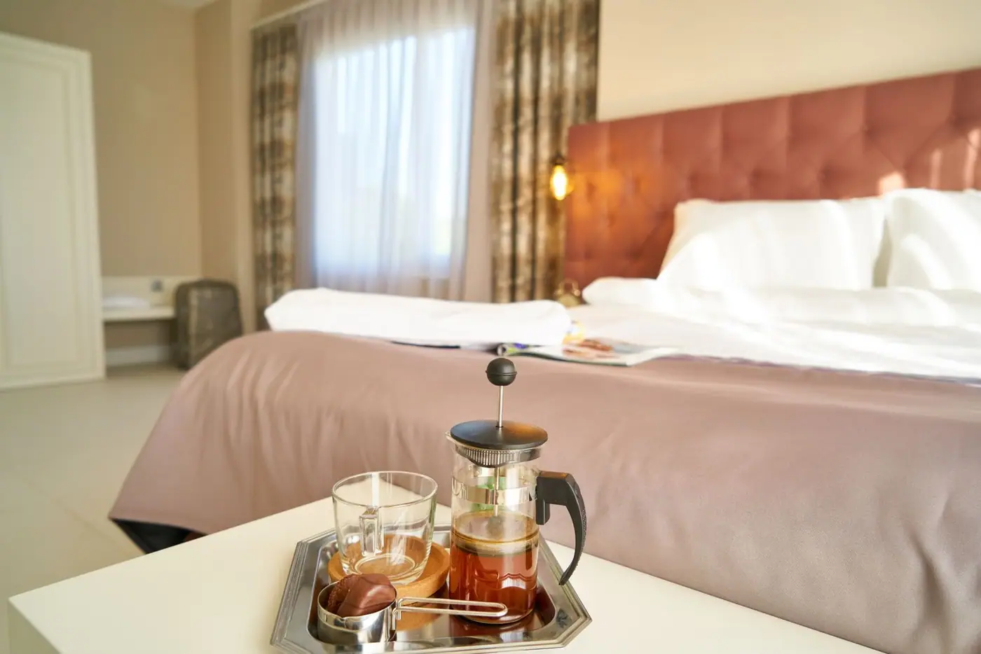 An inviting guest room with a French press coffee set on the bedside table