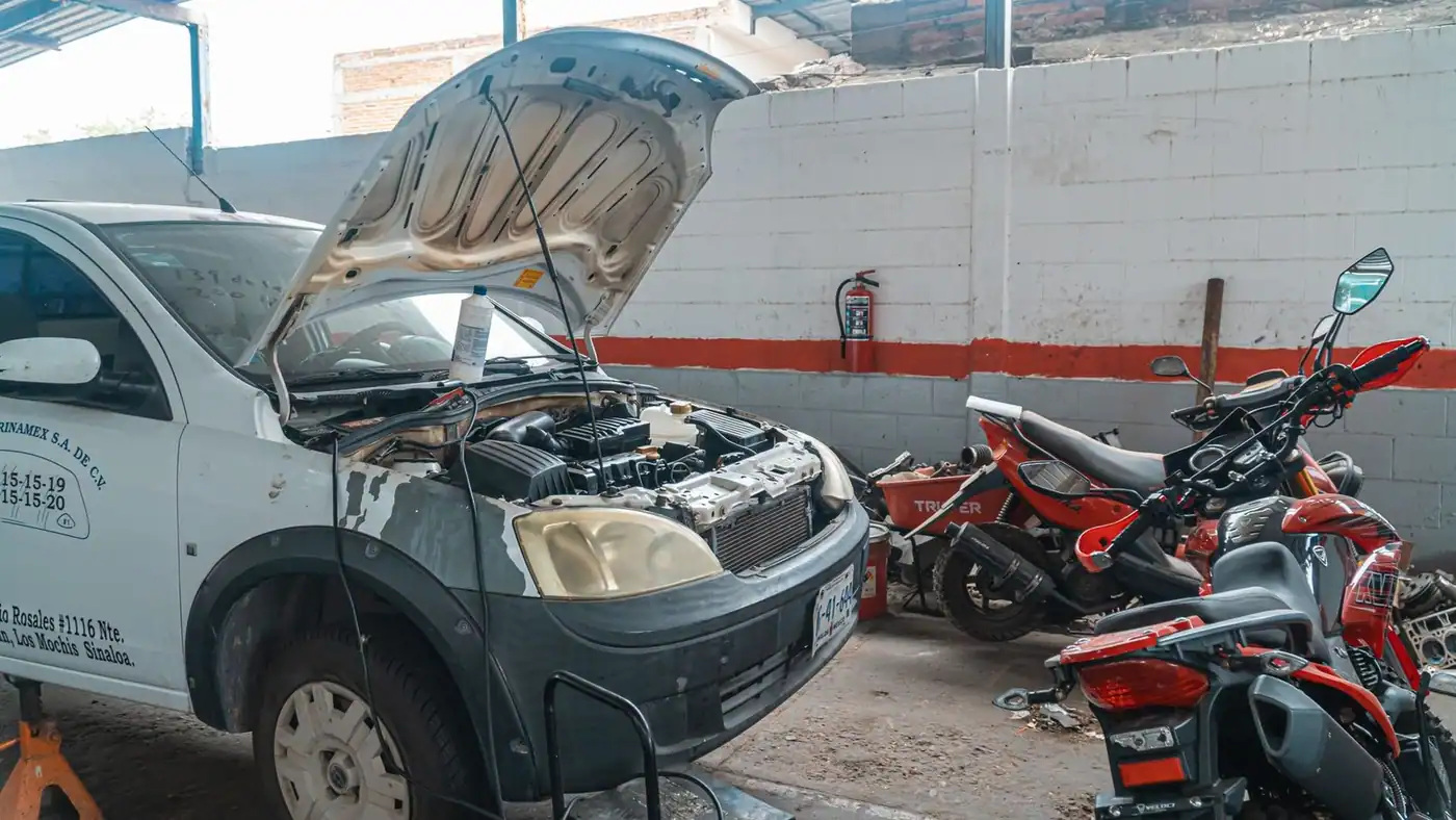 Car being repaired in a garage with motorcycles and tools around.