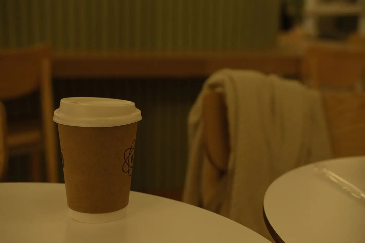 Warm indoor setting featuring a paper coffee cup on a table in a cozy cafe environment.