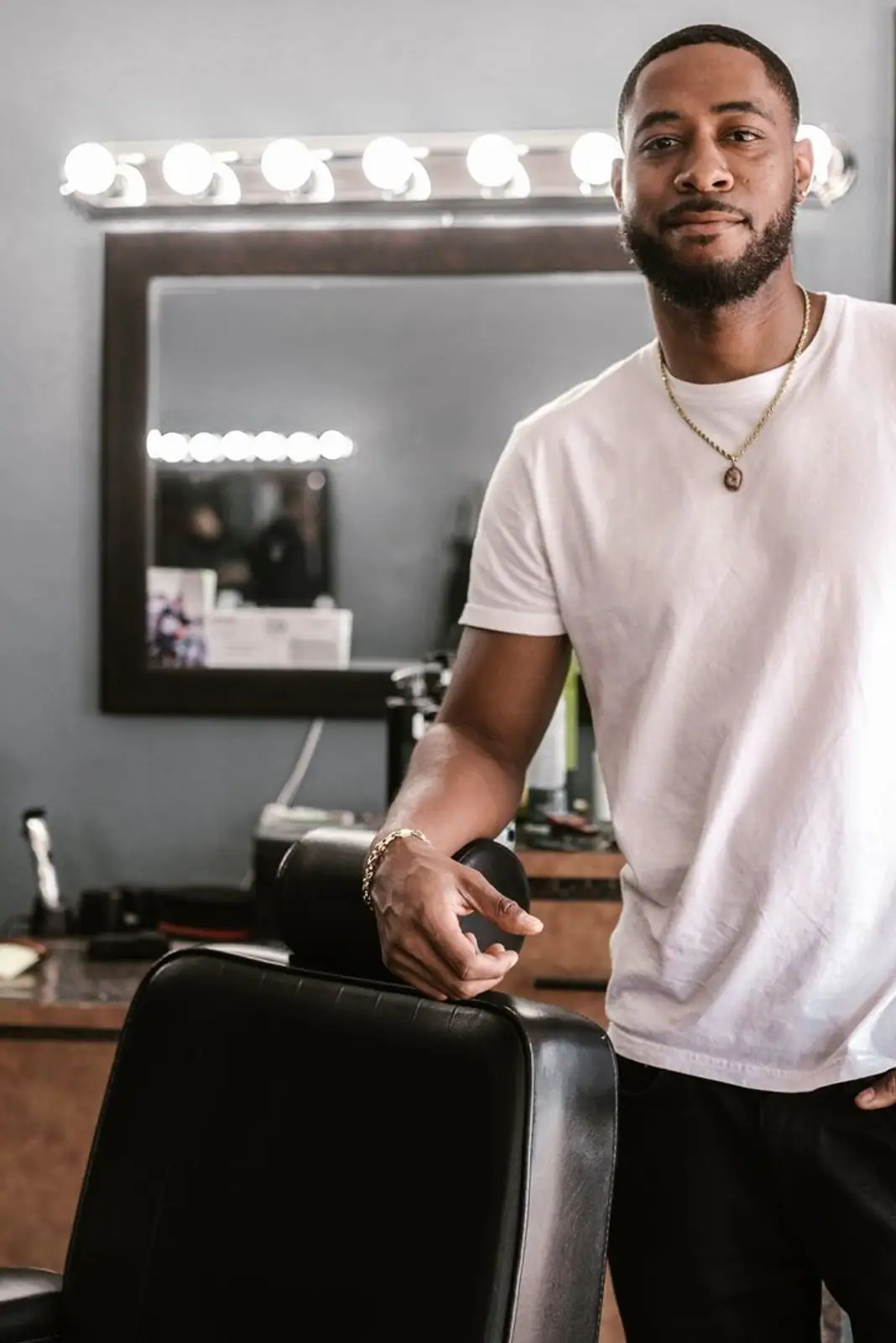 Stylish African American barber stands confidently by a chair in a modern barbershop.