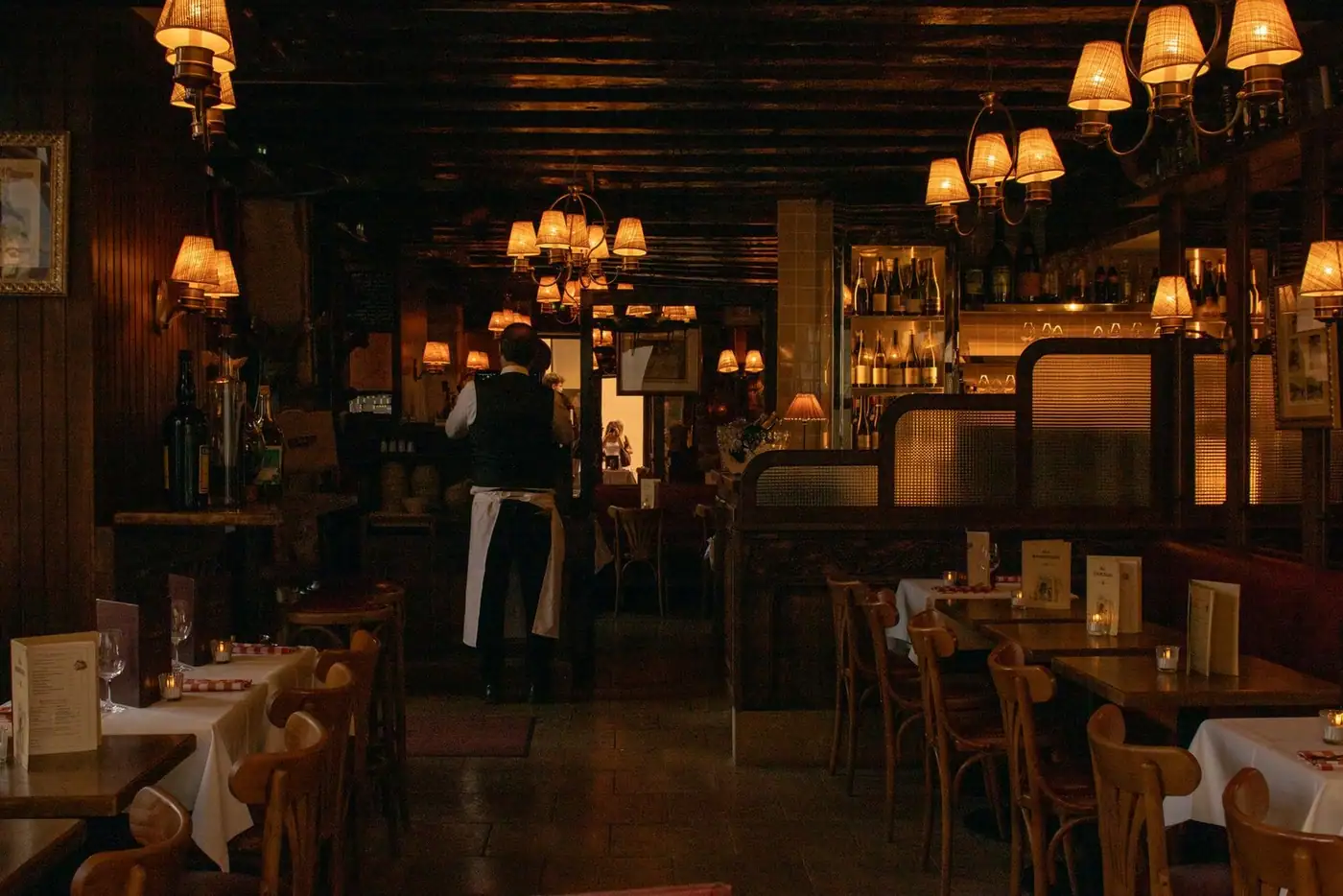 Elegant, dimly lit restaurant interior featuring a waiter and charming wooden decor.