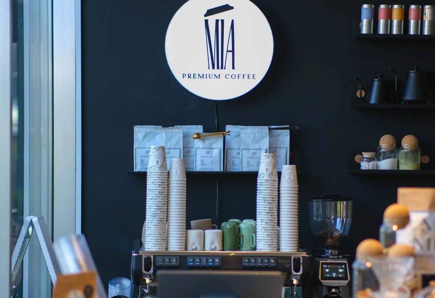 A stylish coffee shop interior featuring premium coffee branding, stacks of cups, and coffee brewing equipment.