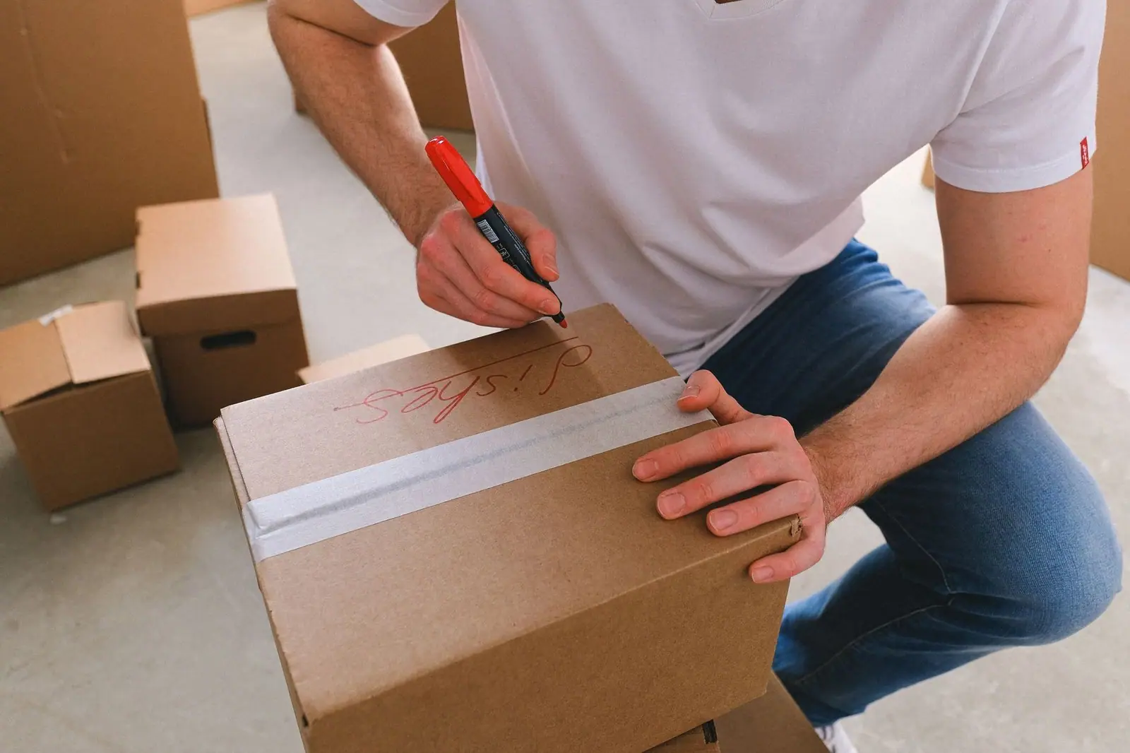 From above of crop unrecognizable male writing on carton box with dishes at home