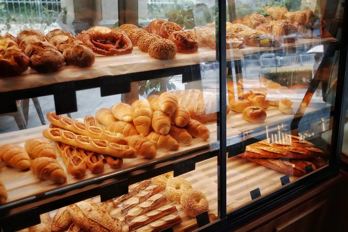 Illuminated glass bakery display case with shelves of breads, rolls, croissants and pastries